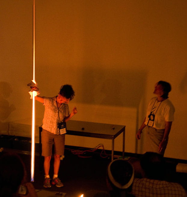 a darkened room with two women -- one holding a long glowing tube