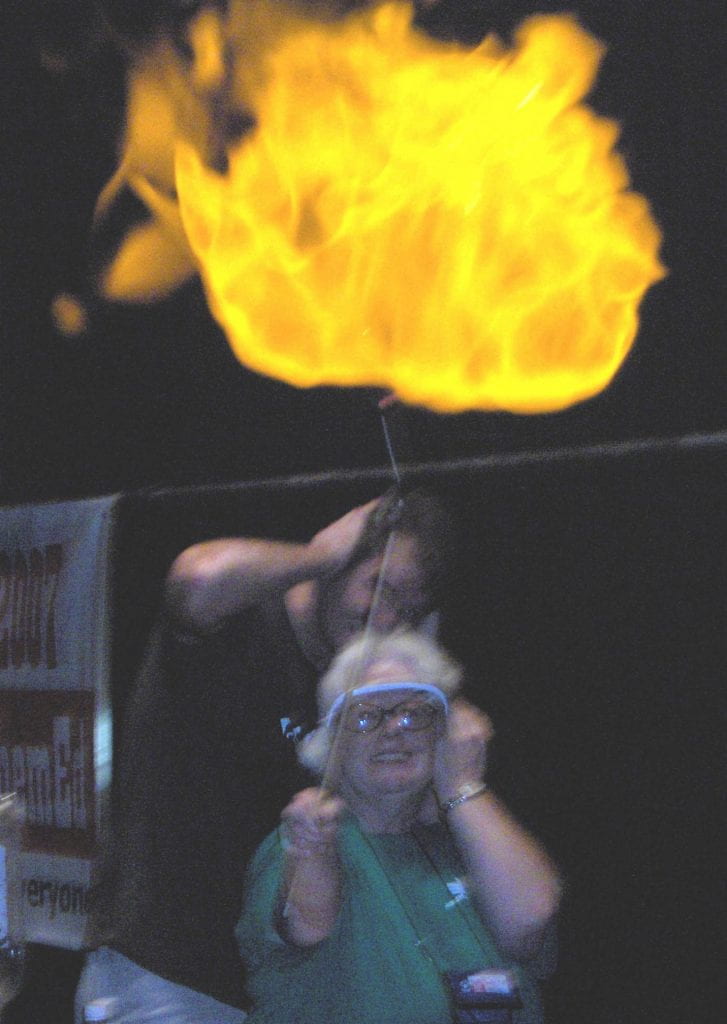 A large flaming ball with two people in goggles holding their ears
