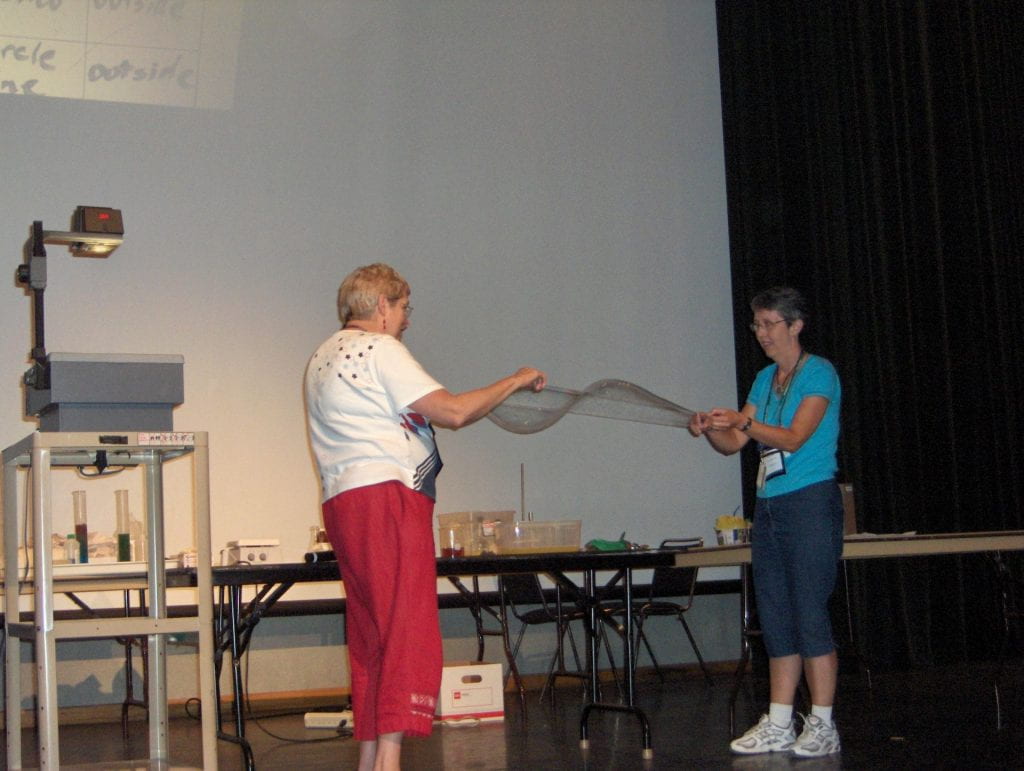 Two women holding string creating a bubble wave
