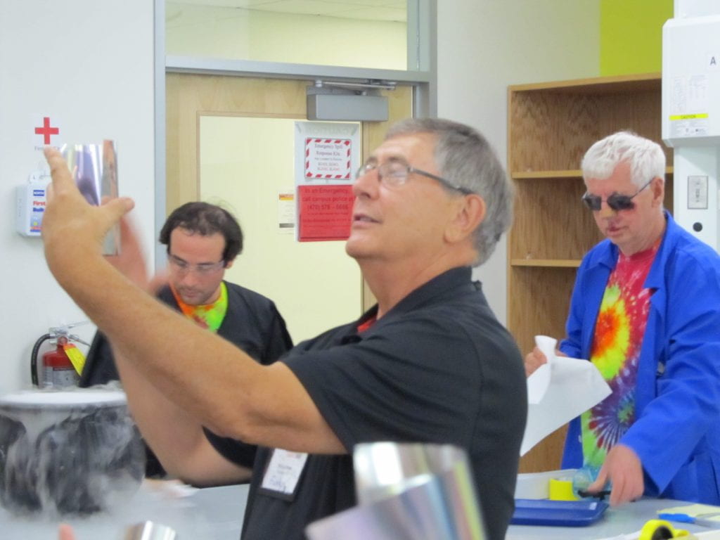 Pat Funk holding up a mirrored paper in a lab setting with ChemEd attendees in the background