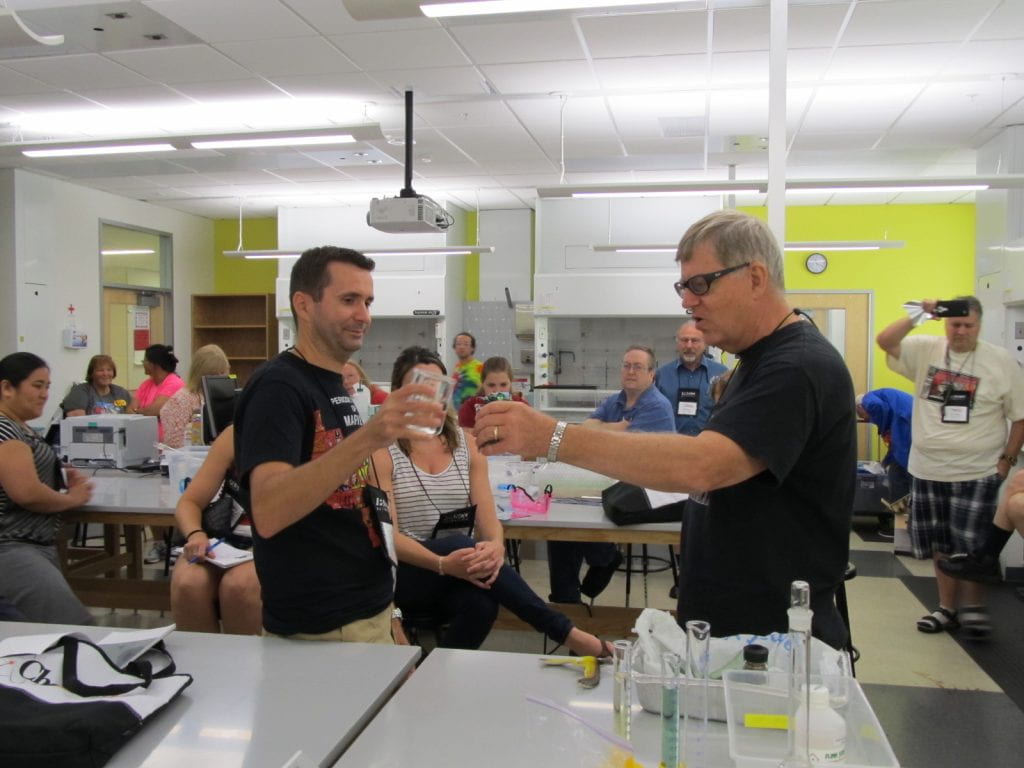 Andy Cherkas holding a beaker with a ChemEd 2015 attendee to do a demo in a lab setting and an audience of about 20 people