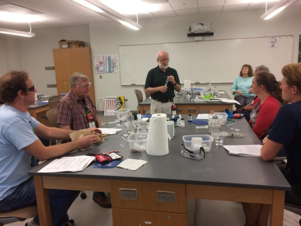 Bill Mattson explaining a demo while holding a syringe in front of a lab room full of attendees