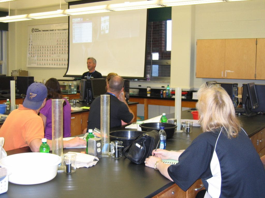 Brian Rohrig in front of a room full of attendees surrounded by high school lab equipment