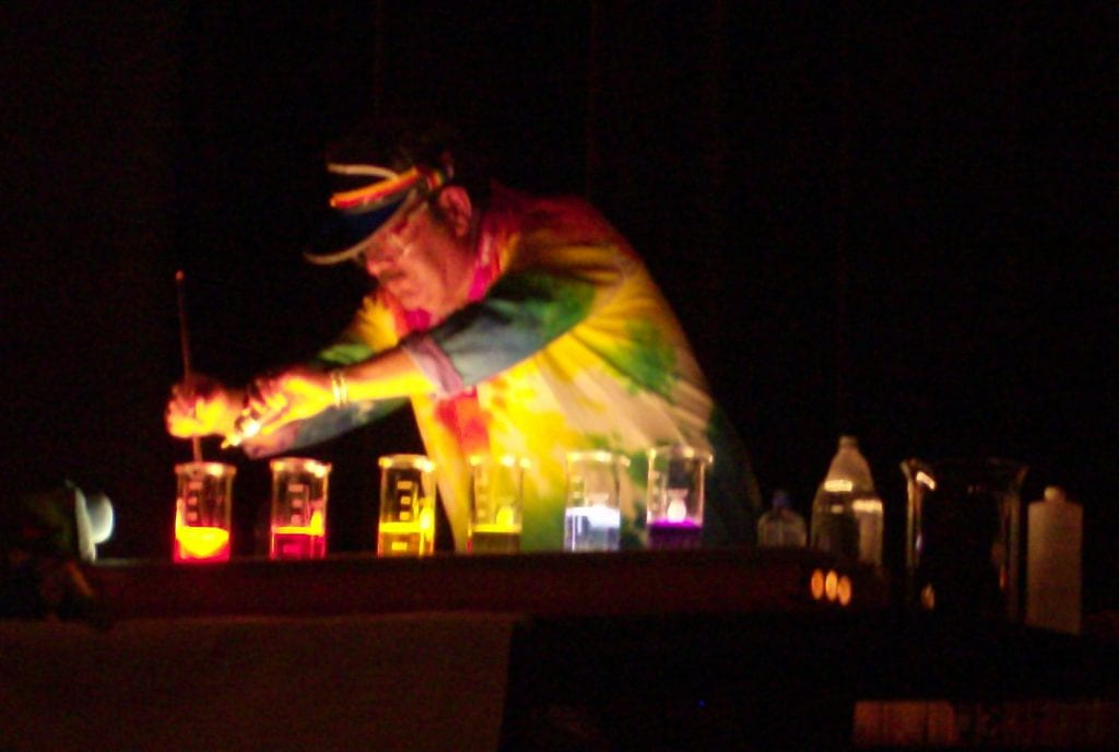 John Fortman presenting a demonstration a darkened room with colourful glowing beakers